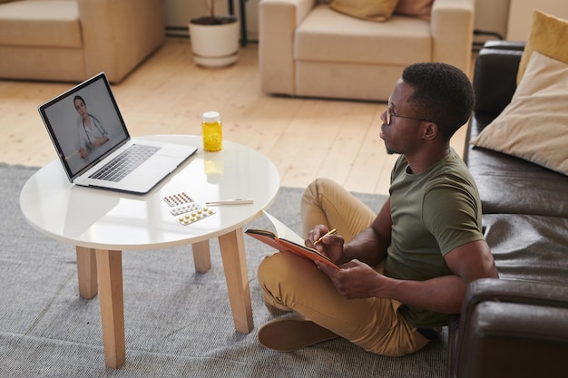 Foto de alto ângulo de um jovem afro-americano adulto sentado em frente ao laptop assistindo médico on-line