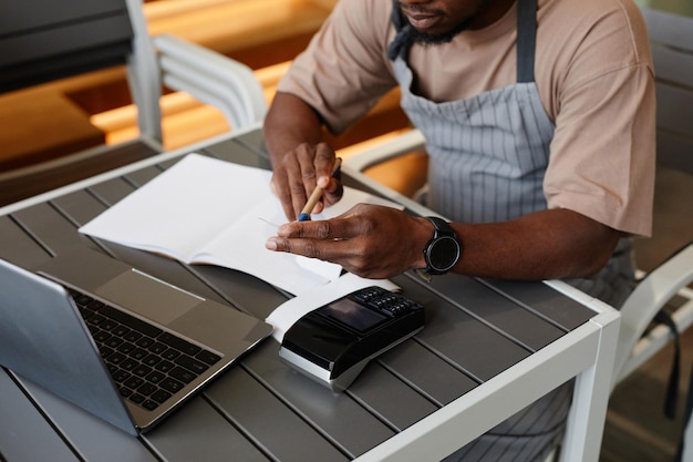 Foto de alto ângulo de um jovem irreconhecível sentado à mesa em frente ao laptop em um pequeno café moderno.