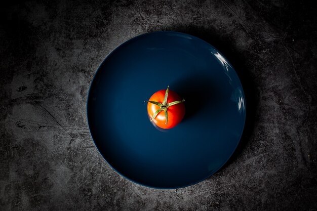 Foto de alto ângulo de um tomate vermelho em um prato azul