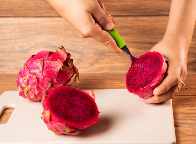 Foto foto de alto ângulo de uma pessoa descascando uma fruta vermelha do dragão com uma colher