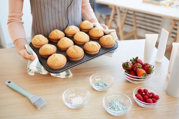 Foto de ângulo alto de uma mulher irreconhecível segurando um molde com cupcakes quentes retirados do forno