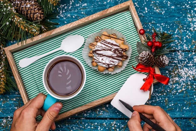 Foto de ano novo de chá com foto de cana de doce e bolos na mesa com ramos de abeto, pessoa escrevendo desejos no cartão