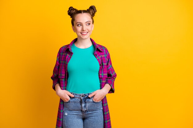 Foto de atraente e encantadora senhora adolescente dois pãezinhos engraçados de mãos dadas, bolsos, bom humor, olhar, lado, espaço vazio, usar, casual, xadrez, longo, magenta, camisa, jeans, isolado, amarela, cor brilhante, fundo