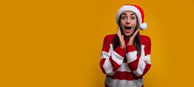 Foto de banner do retrato de uma jovem bonita e animada com chapéu de Papai Noel na época do Natal enquanto ela grita e se diverte em fundo amarelo