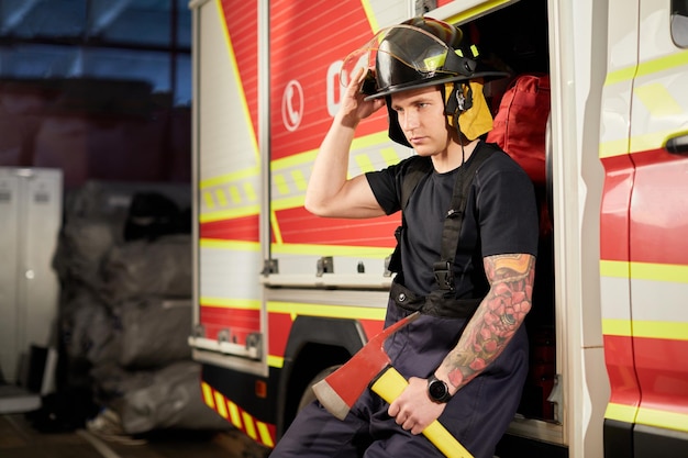 Foto de bombeiro usando capacete com machado contra carro de bombeiros