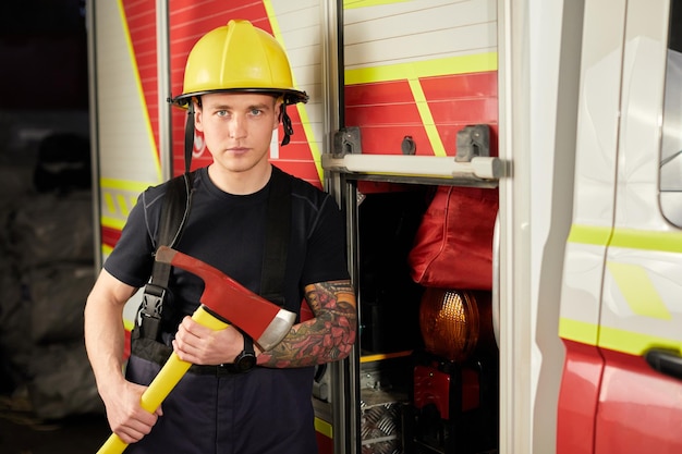 Foto de bombeiro usando capacete com machado contra carro de bombeiros