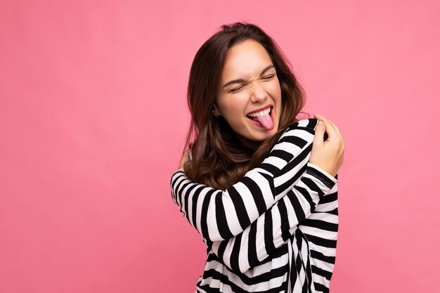 Foto de bonito atraente muito jovem feliz alegre mulher morena vestindo manga comprida listrada casual isolada sobre fundo colorido com espaço de cópia e mostrando a língua.