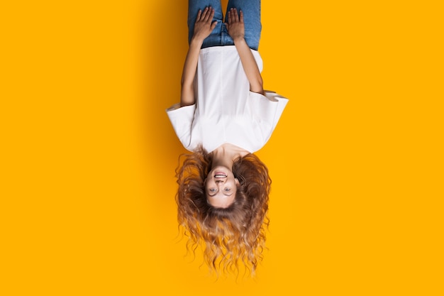 Foto de cabeça para baixo de uma senhora loira de jeans e camiseta branca, sorrindo para a câmera e anunciando algo