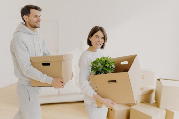 Foto de casal de família carrega caixas grandes com itens domésticos e pertences pessoais se mudam para uma nova casa entram na nova casa comprada ou alugada Proprietários felizes ocupados em desfazer as malas Rotina doméstica