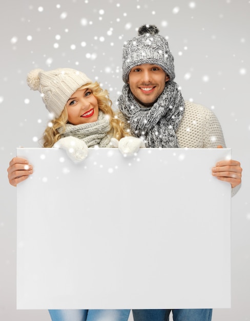 Foto foto de casal de família com roupas de inverno segurando um quadro em branco