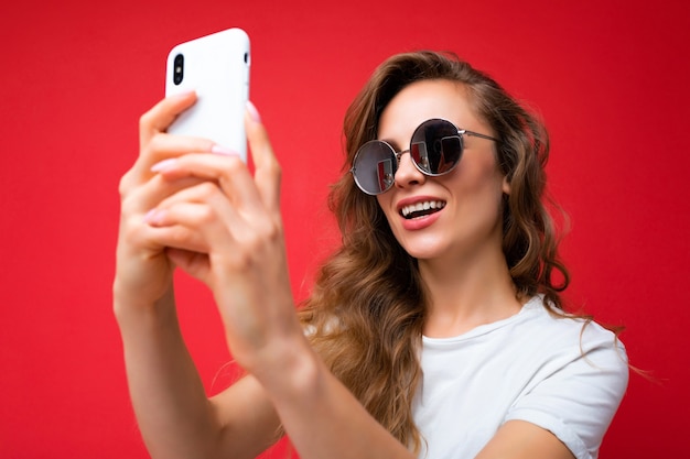 Foto de close da incrível bela jovem loira segurando um telefone celular, tirando uma foto de selfie usando