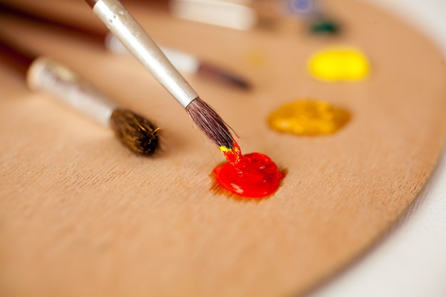 Foto de close de pincel profissional mergulhado em tinta a óleo vermelha na paleta