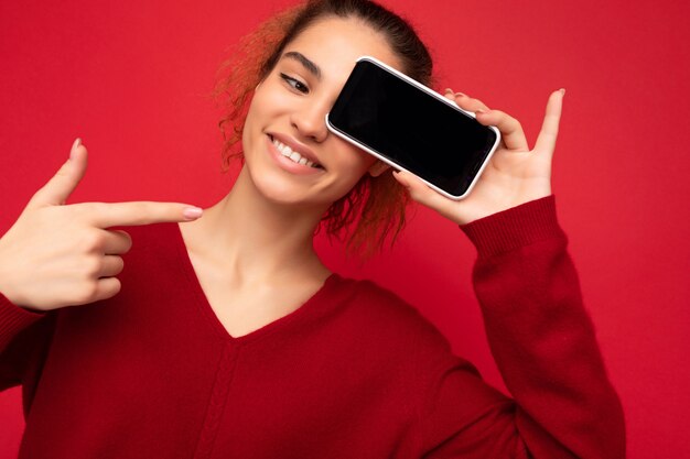 Foto de close de sorridente jovem engraçada feliz vestindo um suéter vermelho escuro isolado sobre o vermelho