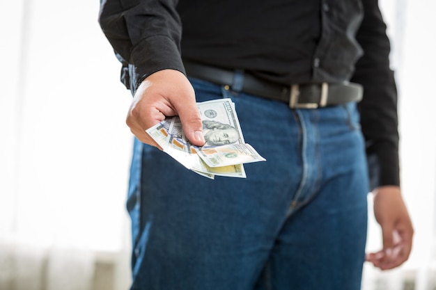 Foto de close de um homem de jeans e camisa segurando notas de cem dólares