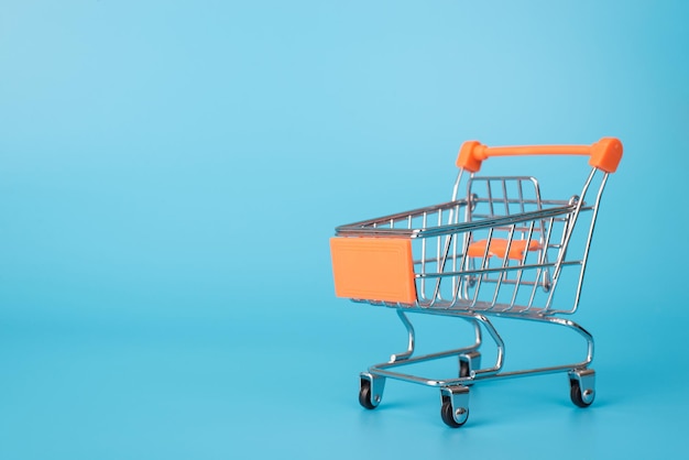 Foto de close de um pequeno carrinho de compras com alça laranja isolado sobre fundo azul claro com espaço em branco