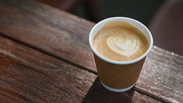 Foto de close-up da caneca de café com leite Take away colocada sobre uma mesa de madeira.