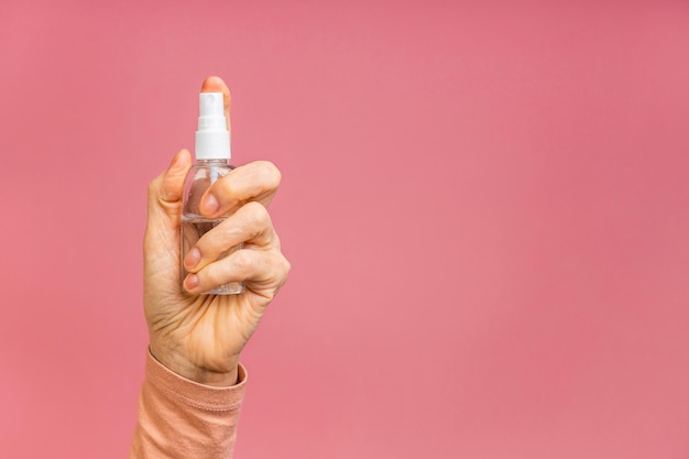 Foto de close-up da mão de mulher envelhecida madura sênior segurando desinfetante spray lavagem limpeza mãos saúde quarentena isolada sobre fundo rosa.