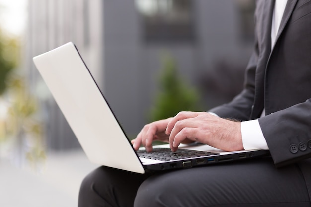 Foto de close-up da mão de um empresário em um terno trabalhando em um laptop branco