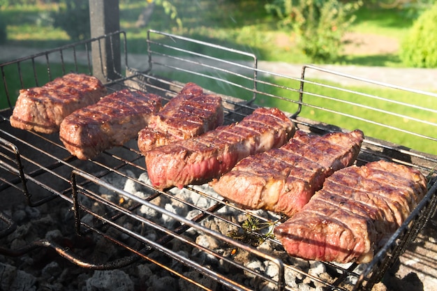 Foto de close up de carne grelhada média em uma grade. Bifes de churrasco no braseiro com fumaça natural. Cozinhar ao ar livre.