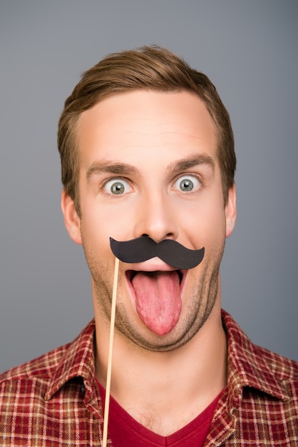 Foto de close-up de homem com bigode de papel mostrando a língua