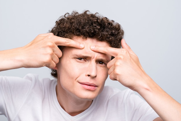 Foto de close-up de jovem moreno encaracolado checando acnes no rosto isoladas em cinza