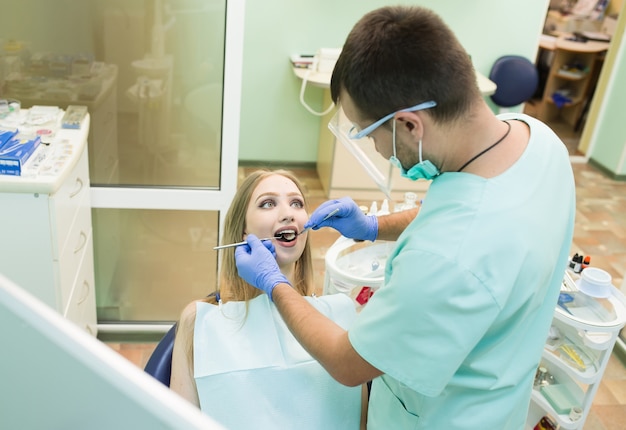 Foto de close-up de jovem sentado na cadeira do dentista com a boca aberta no consultório do dentista enquanto faz o exame.