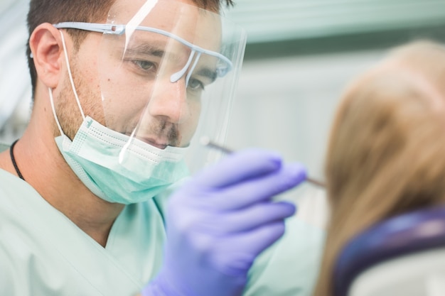 Foto de close-up de jovem sentado na cadeira do dentista com a boca aberta no consultório do dentista enquanto faz o exame.