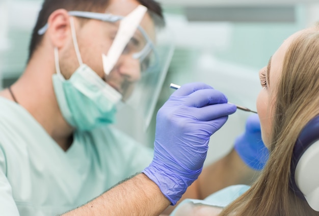 Foto de close-up de jovem sentado na cadeira do dentista com a boca aberta no consultório do dentista enquanto faz o exame.