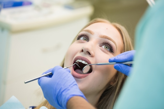 Foto de close-up de jovem sentado na cadeira do dentista com a boca aberta no consultório do dentista enquanto faz o exame.