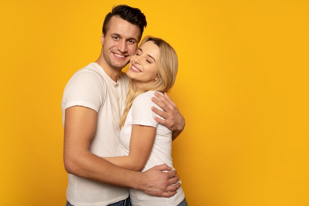 Foto de close-up de um casal fofo, abraçando-se com força e sorrindo enquanto posava em um fundo amarelo