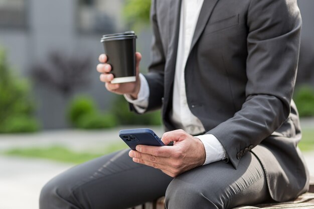 Foto de close-up de um empresário correspondendo ao telefone em um terno de negócio, as mãos de um homem segurando uma xícara e um telefone