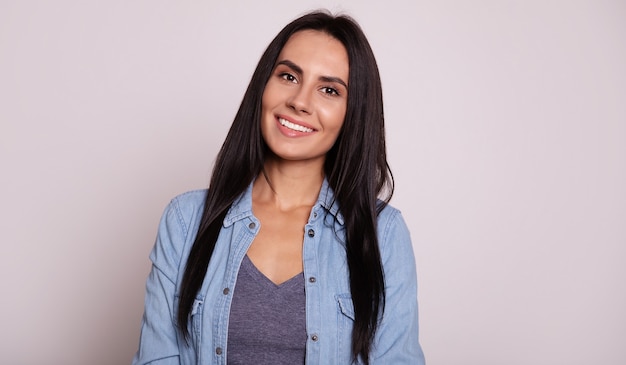 Foto foto de close-up de uma jovem e linda garota em roupa casual, que está posando com os braços cruzados, olhando para a câmera e sorrindo amplamente