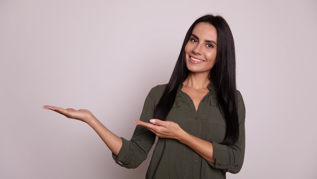 Foto de close-up de uma linda garota de cabelos escuros com um largo sorriso, que está olhando para a câmera e mostrando os polegares para cima com a mão esquerda e fingindo estar segurando algo na mão direita.