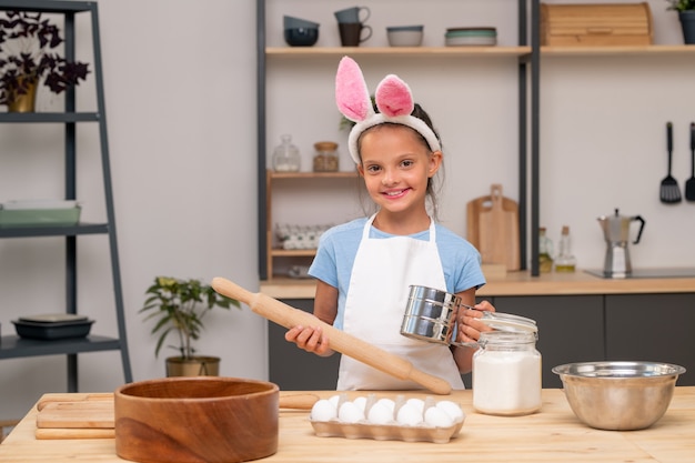 Foto de close-up de uma menina procurando receita de salada em tablet digital enquanto está de pé na mesa da cozinha de madeira