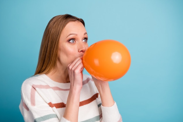 Foto de close-up de uma mulher alegre positiva fofa se sentindo como uma criança soprando uma bola de ar, olhando para o espaço vazio, parede de cor azul pastel