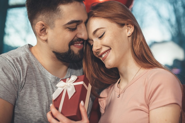 Foto de close-up de uma senhora ruiva com sardas segurando um presente do amante e sorrindo abraçados