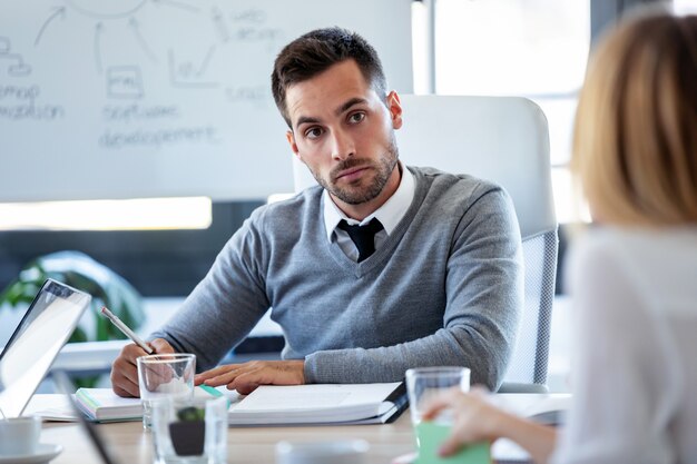 Foto de concentrado jovem empresário ouvindo seu parceiro e fazendo anotações no espaço de coworking.