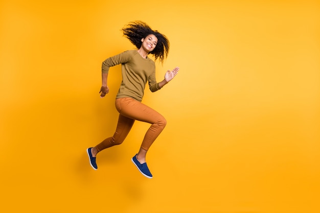 Foto de corpo inteiro de alegre positivo linda atraente encantadora linda garota vestindo calças laranja correndo pulando em direção ao espaço vazio isolado sobre um fundo de cor vívida