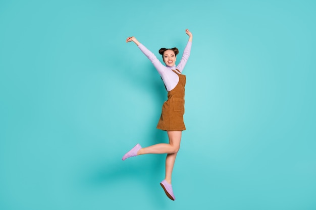 Foto de corpo inteiro de animada deliciosa senhora sortuda campeã hooray salto levantar mãos gesto inovador usar dois pãezinhos tênis roxos outono mini vestido marrom na moda isolado fundo de cor verde-azulado