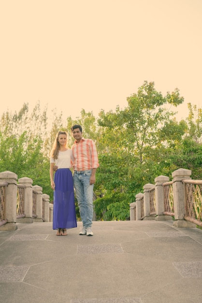 Foto de corpo inteiro de casal multiétnico juntos e apaixonados na ponte do pacífico parque verde