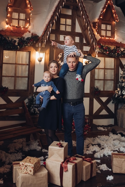 Foto de corpo inteiro de família feliz de mãe, pai e dois filhos em pé em uma sala decorada com presentes de natal sob a neve