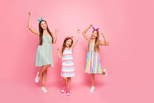 Foto de corpo inteiro de garotas alegres cortando cabelo comprido com bandanas levantando os punhos gritando sim celebrando a vitória usar vestido de saia isolado sobre fundo rosa