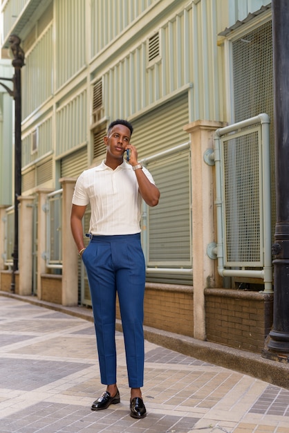 Foto de corpo inteiro de jovem empresário africano falando ao ar livre no celular