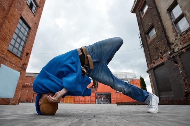 Foto de corpo inteiro de jovem fazendo pose de breakdance em fábrica urbana ao ar livre e escondendo fac