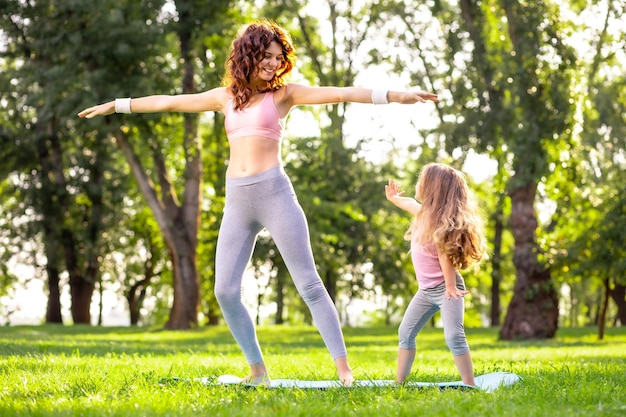 Foto de corpo inteiro de mãe e filha em pé em ioga posando no parque