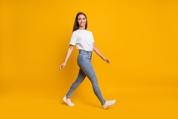 Foto de corpo inteiro de menina dando um passo à frente olhando copyspace sorrindo isolada em um fundo de cor amarela brilhante