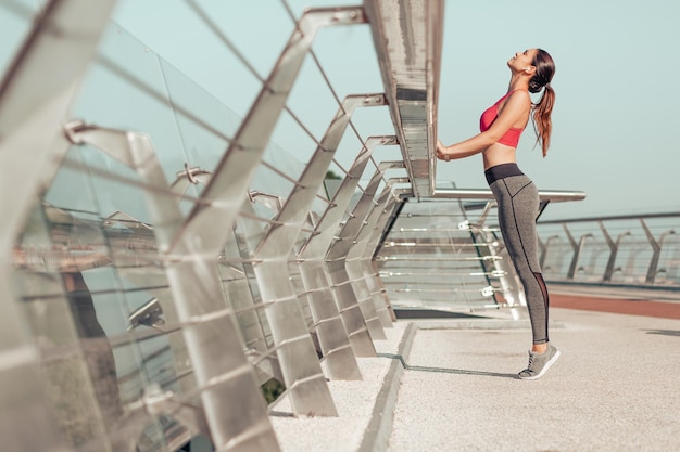 Foto de corpo inteiro de mulher esportiva se aquecendo na ponte pela manhã