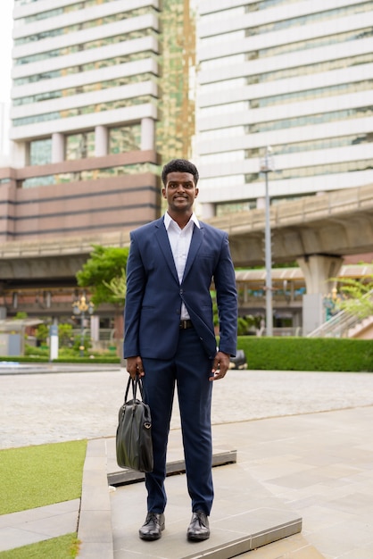 Foto de corpo inteiro de um empresário africano ao ar livre na cidade, sorrindo, foto vertical