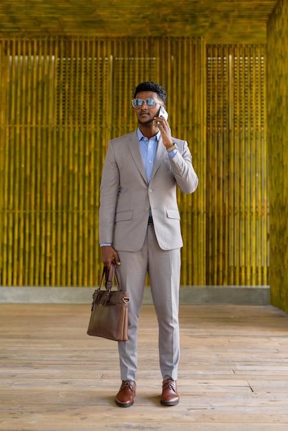 Foto de corpo inteiro de um empresário africano ao ar livre usando telefone celular