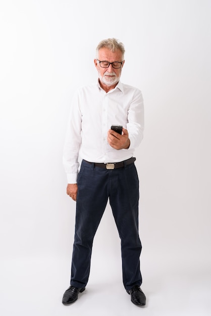 Foto de corpo inteiro de um homem barbudo sênior bonito em pé no celular branco